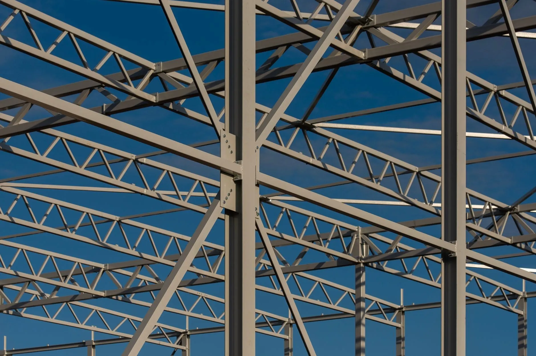 A steel roof frame of trusses and columns against a deep blue sky