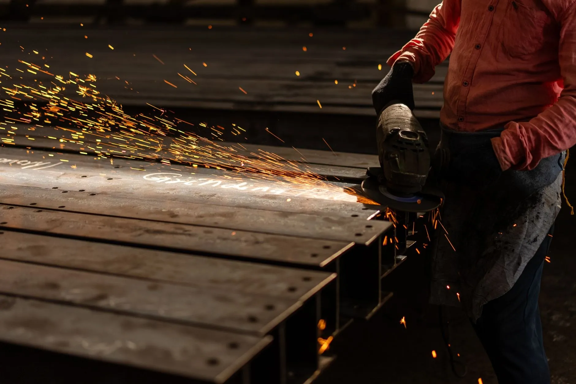 A fabricator grinding the end of a steel beam, sparks spraying across the plate