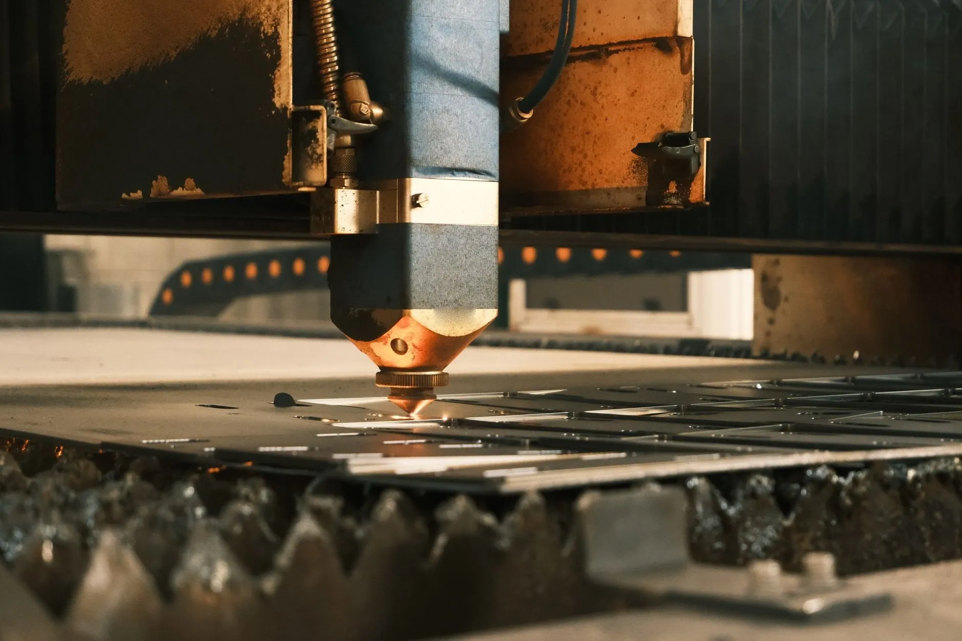 The nozzle of a fibre laser cutting head just above a steel sheet on the slatted bed