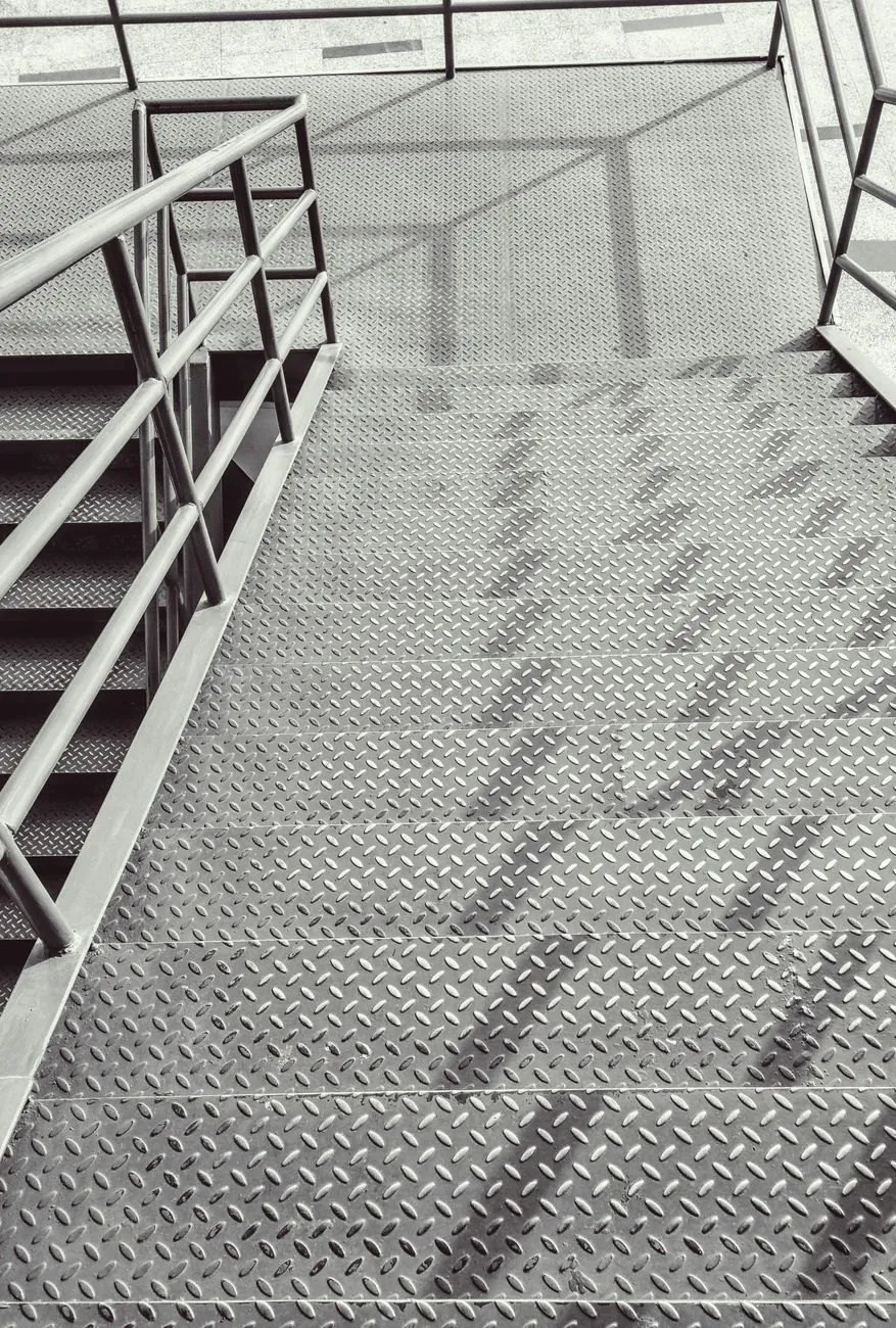 Looking down a steel stair with chequer-plate treads and a tubular handrail