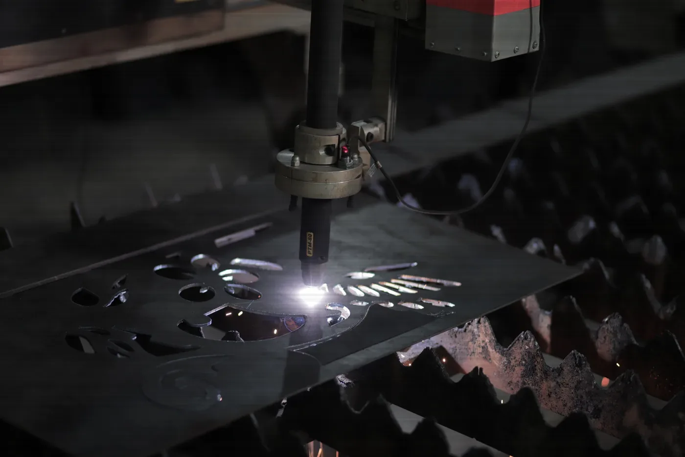 A plasma head cutting parts out of a steel plate, the arc lighting the cut