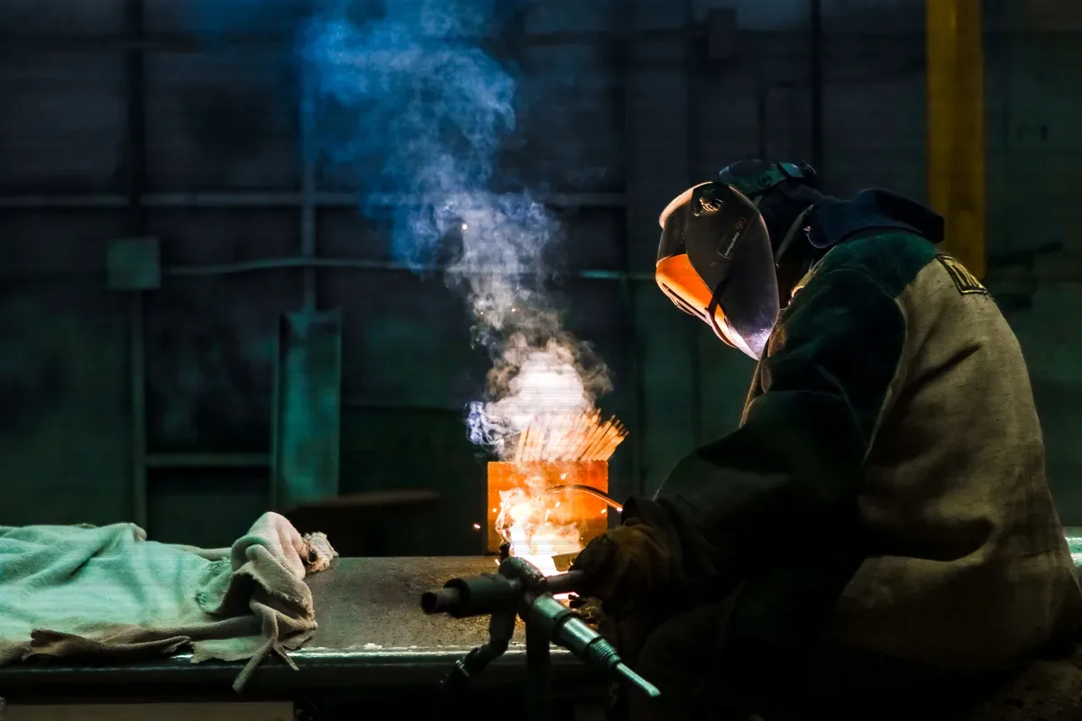 A coded welder working in a welding bay, the arc lighting the plate in front of them